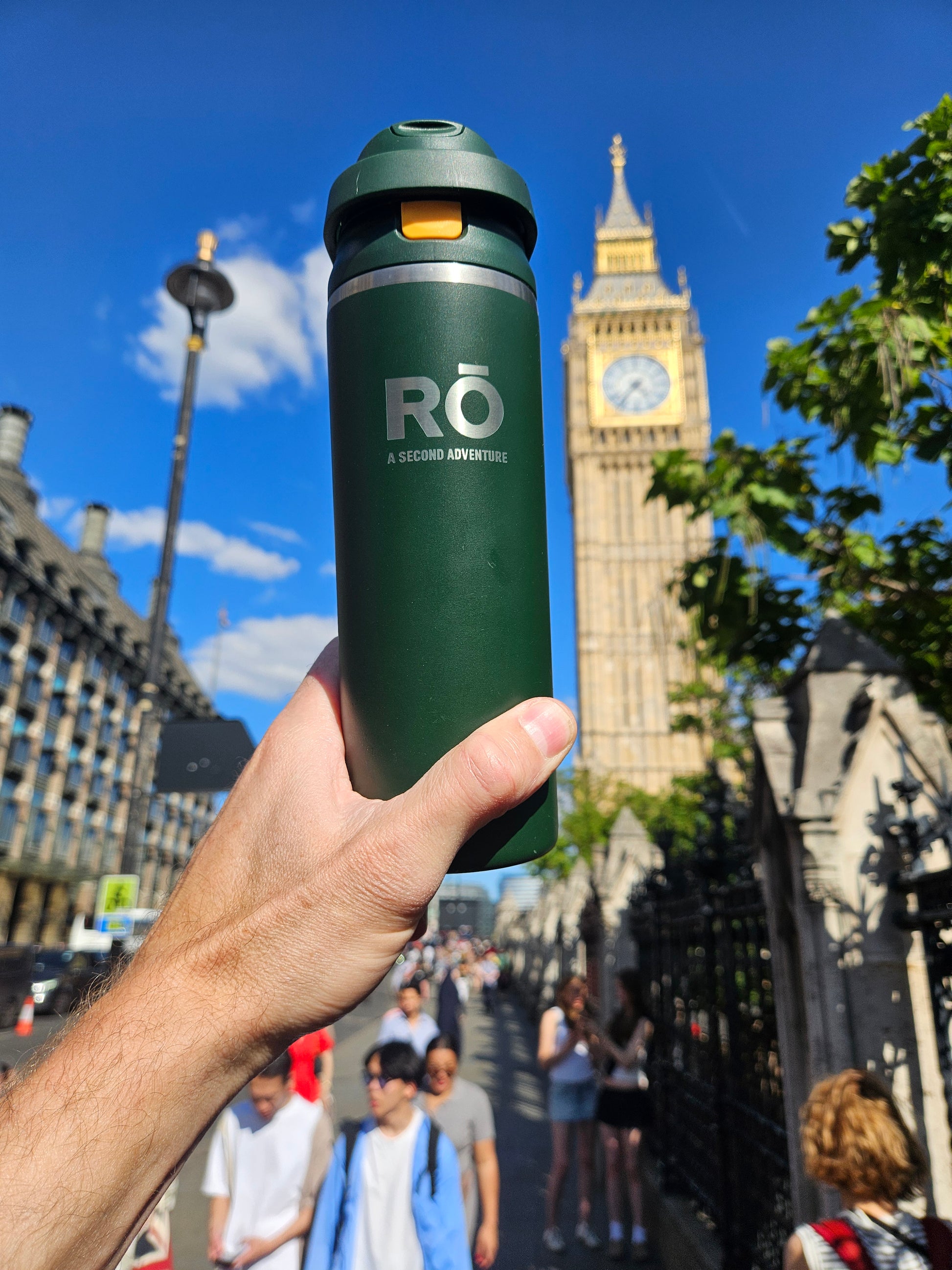 A hand holds a dark green insulated water bottle with the brand logo 'RO' (A Secondo Argentine) in front of a blurred background of Big Ben and London street scene.